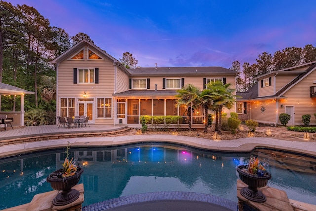pool at dusk with a deck, outdoor dining space, a sunroom, and an outdoor pool