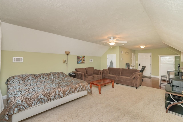 carpeted bedroom with a ceiling fan, visible vents, vaulted ceiling, and a textured ceiling