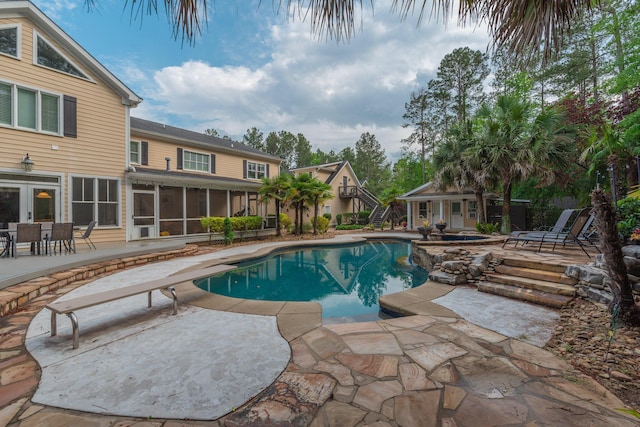 pool with an outdoor structure, a sunroom, a diving board, and a patio area