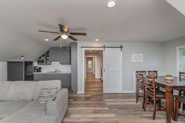 dining space featuring a barn door, ceiling fan, light wood-style floors, baseboards, and recessed lighting