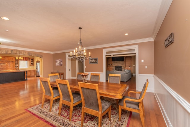 dining space featuring a fireplace, light wood-type flooring, a wainscoted wall, and a notable chandelier