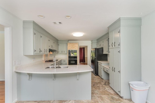 3411 Kamel Cir, Augusta, GA 30909 - kitchen featuring a peninsula, black appliances, light countertops, a breakfast bar, and under cabinet range hood