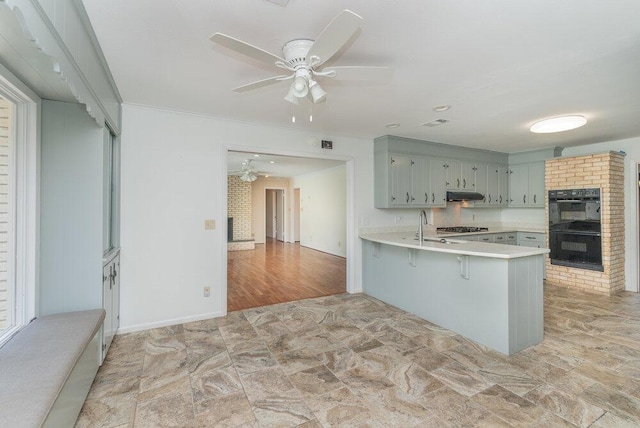 3411 Kamel Cir, Augusta, GA 30909 - kitchen featuring a fireplace, under cabinet range hood, ceiling fan, a peninsula, and light countertops