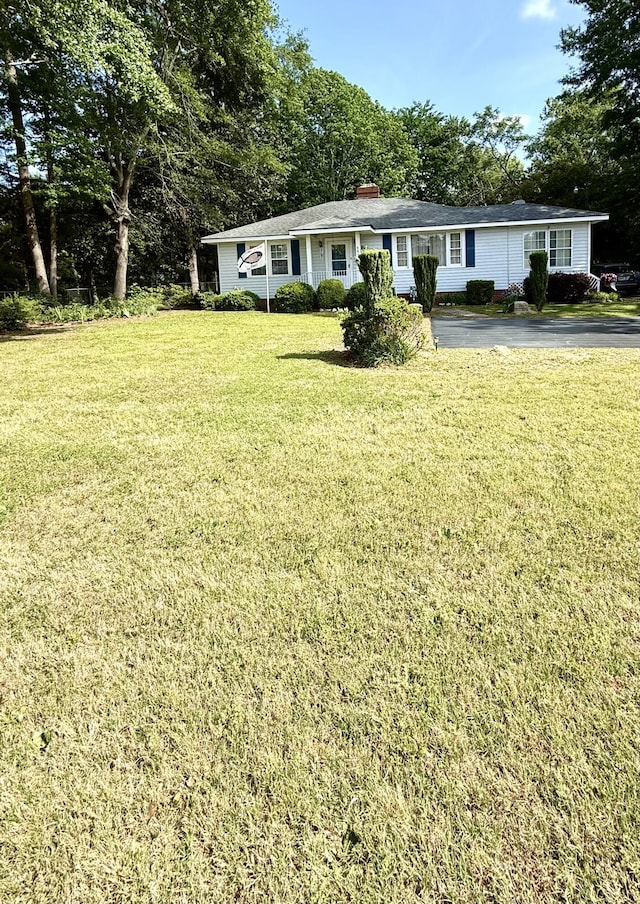 view of front facade featuring aphalt driveway, a front lawn, and a chimney