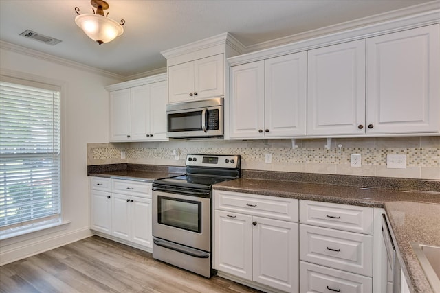 kitchen with appliances with stainless steel finishes, white cabinets, light wood-style flooring, crown molding, and dark countertops