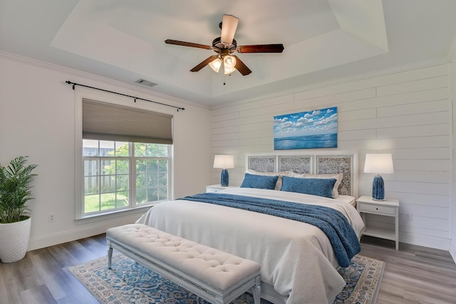 bedroom with a raised ceiling, wood finished floors, baseboards, wood walls, and a ceiling fan