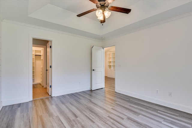unfurnished bedroom featuring a tray ceiling, light wood-style flooring, baseboards, and ornamental molding