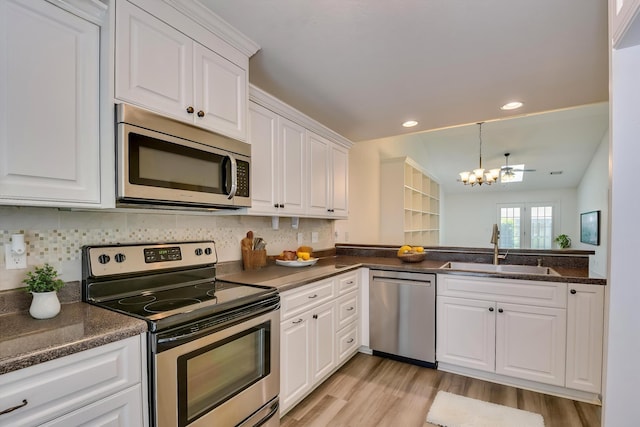 kitchen with stainless steel appliances, a sink, a chandelier, dark countertops, and light wood-style flooring