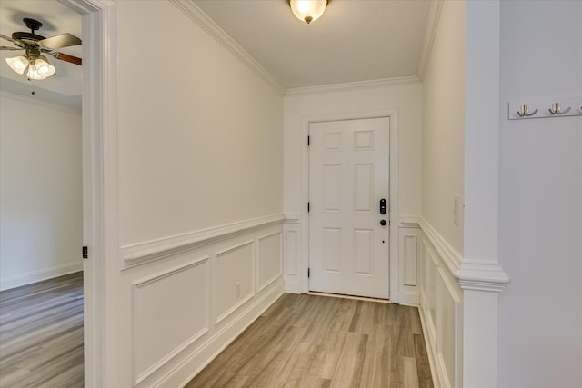 doorway to outside featuring light wood-type flooring, ornamental molding, ceiling fan, and a wainscoted wall