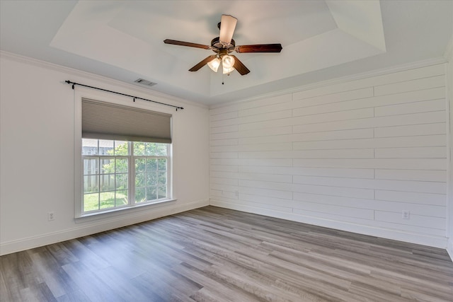 spare room with a tray ceiling, ceiling fan, wood finished floors, baseboards, and ornamental molding