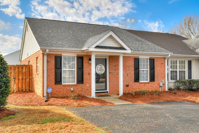 view of front of house with roof with shingles, brick siding, and fence