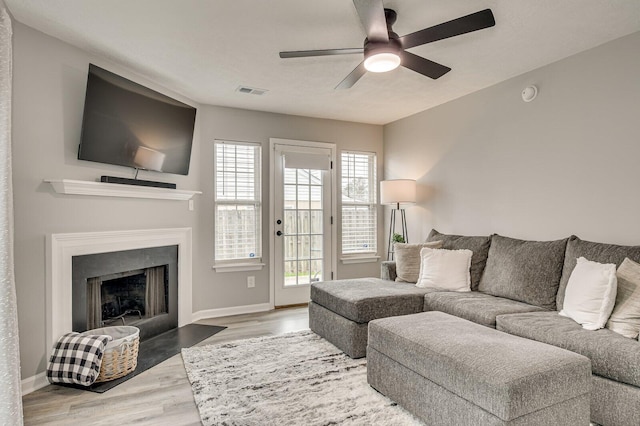 living area featuring a fireplace with flush hearth, wood finished floors, a ceiling fan, and baseboards