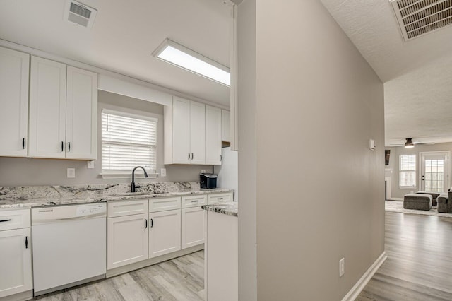 kitchen with white cabinets, visible vents, white dishwasher, and a sink