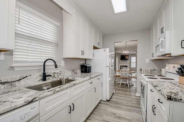 kitchen featuring white appliances, white cabinets, light stone countertops, light wood-type flooring, and a sink