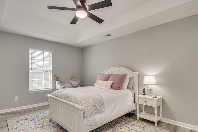 bedroom with light wood-style floors, baseboards, visible vents, and a tray ceiling