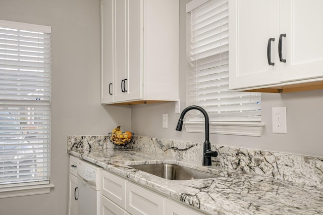 kitchen with light stone counters, white dishwasher, a sink, and white cabinetry