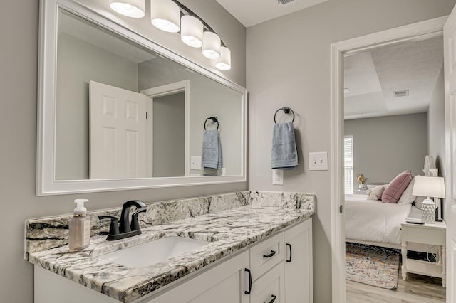 ensuite bathroom featuring vanity, ensuite bath, wood finished floors, and visible vents