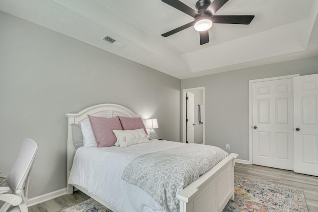 bedroom with a raised ceiling, visible vents, light wood-style floors, a ceiling fan, and baseboards