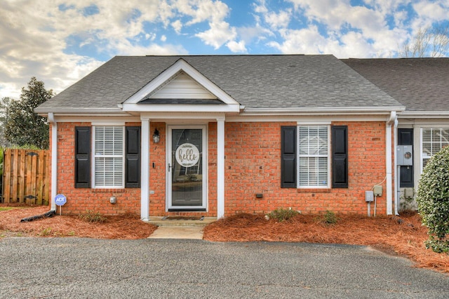 bungalow-style home featuring brick siding, roof with shingles, and fence