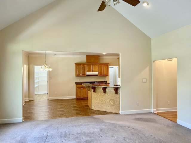 unfurnished living room with baseboards, dark carpet, ceiling fan with notable chandelier, and high vaulted ceiling