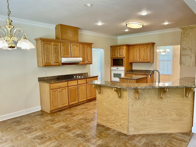 kitchen with crown molding, oven, a breakfast bar area, a chandelier, and under cabinet range hood