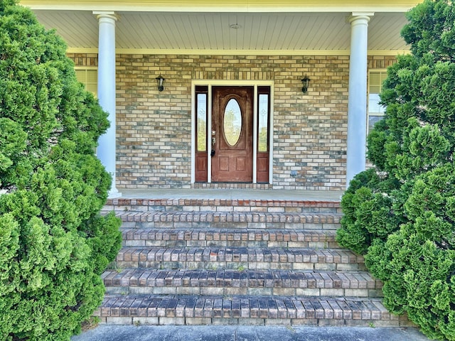 doorway to property featuring covered porch and brick siding