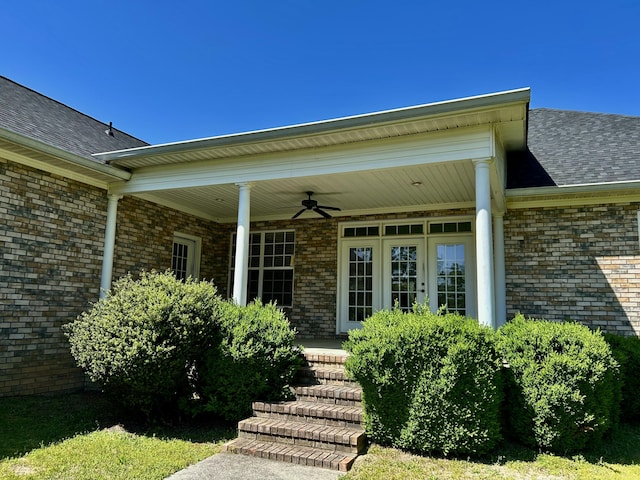 doorway to property featuring brick siding, ceiling fan, roof with shingles, and covered porch