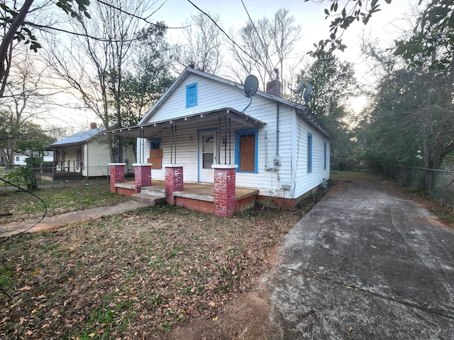 view of front of home featuring covered porch, a chimney, and fence