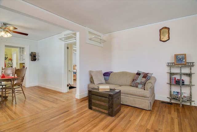 living area with crown molding, light wood finished floors, a ceiling fan, and baseboards