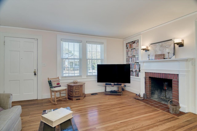 living area featuring light wood-style floors, a brick fireplace, ornamental molding, and built in shelves