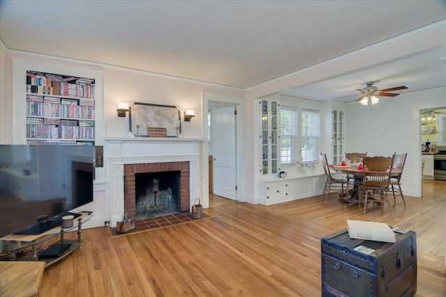 living area featuring a brick fireplace, ceiling fan, and wood finished floors