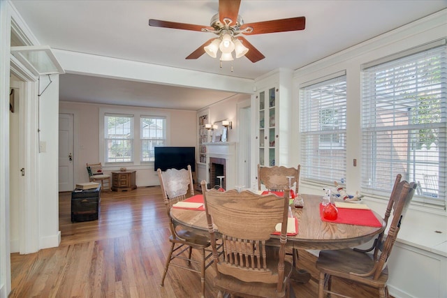 dining area featuring light wood-type flooring, a brick fireplace, and a ceiling fan