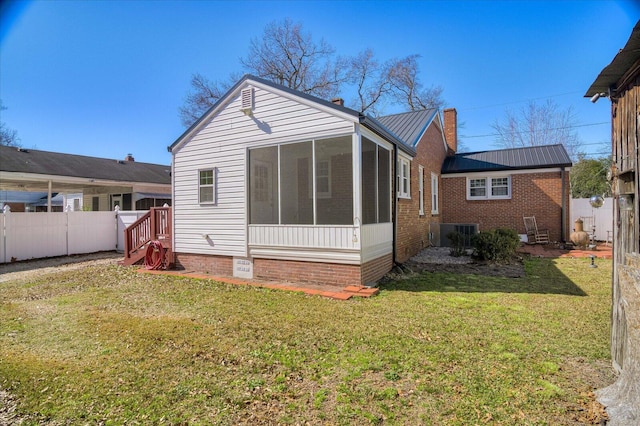 back of house featuring a lawn, a chimney, a fenced backyard, and a sunroom