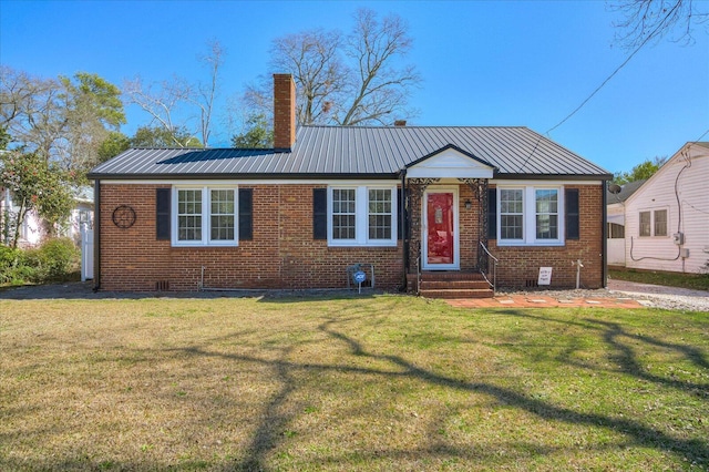 view of front of house with a front yard, a chimney, metal roof, and brick siding