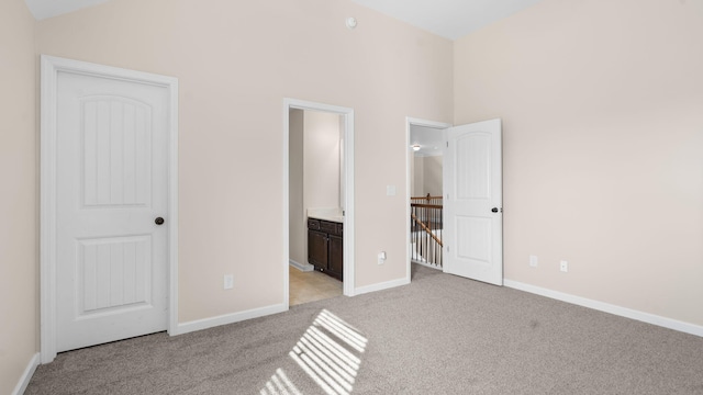 unfurnished bedroom with light carpet, a closet, a towering ceiling, and ensuite bath