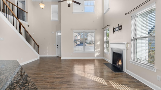 unfurnished living room with ceiling fan, dark wood-type flooring, and a high ceiling