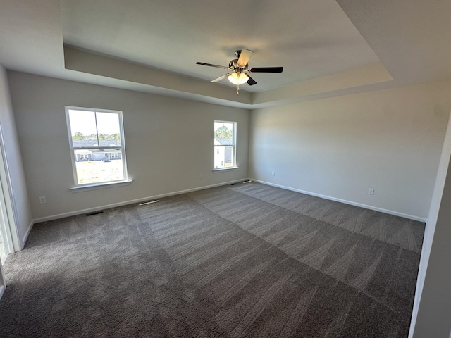 spare room featuring a raised ceiling, baseboards, and dark colored carpet