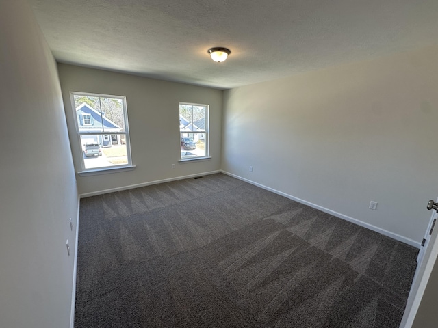 spare room featuring visible vents, baseboards, a textured ceiling, and dark carpet