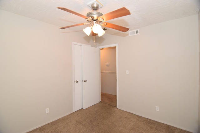 spare room with a textured ceiling, carpet floors, ceiling fan, and visible vents