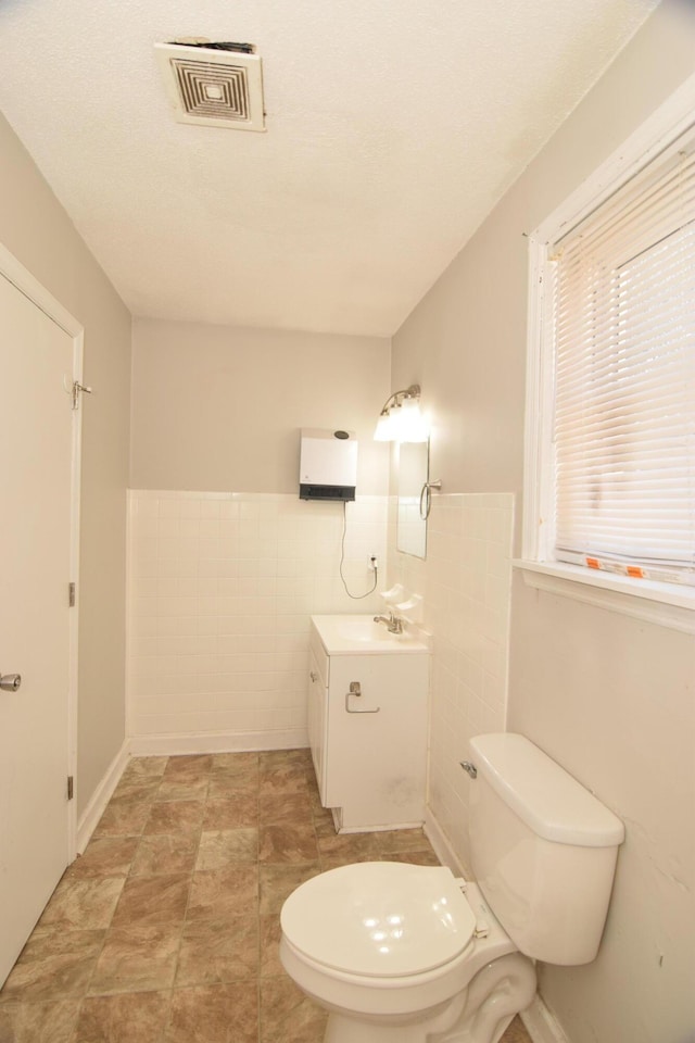 half bath featuring toilet, a wainscoted wall, vanity, visible vents, and tile walls