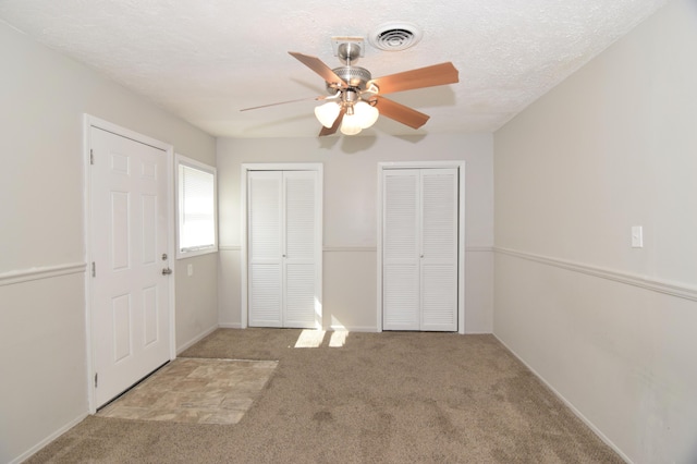 unfurnished bedroom featuring carpet flooring, visible vents, a textured ceiling, and two closets