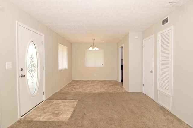 foyer with a notable chandelier, a textured ceiling, visible vents, and light colored carpet