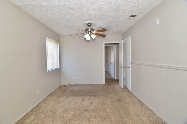 spare room with light carpet, a textured ceiling, visible vents, and a ceiling fan