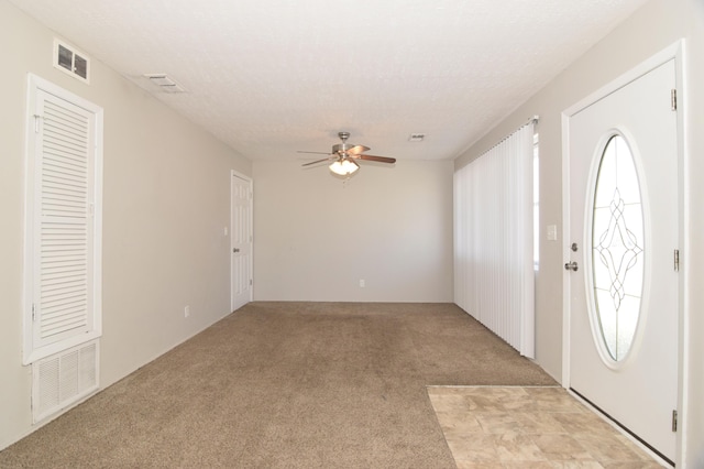 entrance foyer featuring light carpet, ceiling fan, visible vents, and a textured ceiling