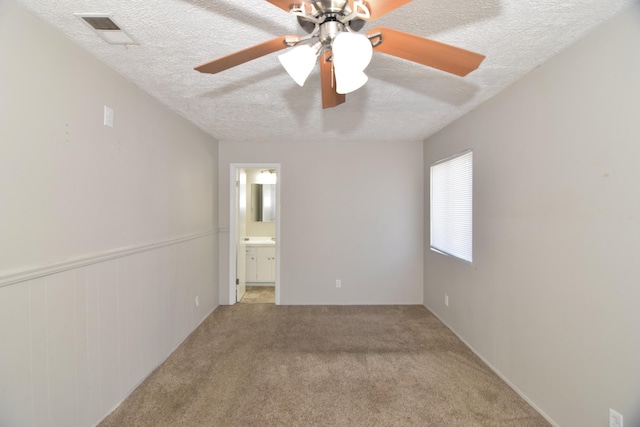 unfurnished room featuring a textured ceiling, ceiling fan, light colored carpet, visible vents, and wainscoting