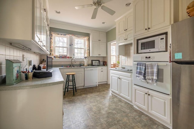 kitchen with sink, white appliances, white cabinetry, ornamental molding, and decorative backsplash