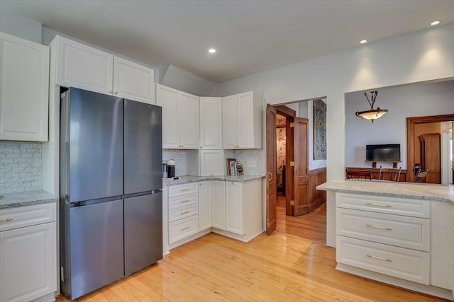 kitchen featuring white cabinetry, decorative backsplash, light hardwood / wood-style flooring, and stainless steel refrigerator