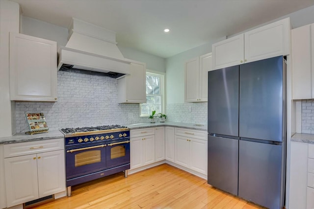 kitchen with stainless steel refrigerator, double oven range, custom range hood, white cabinets, and decorative backsplash