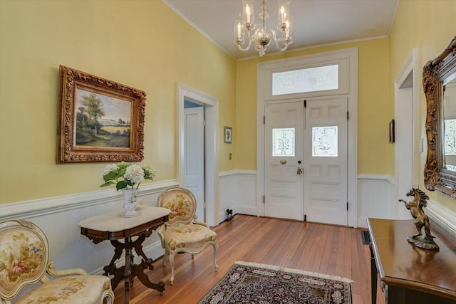 entryway with a notable chandelier, ornamental molding, and light wood-type flooring