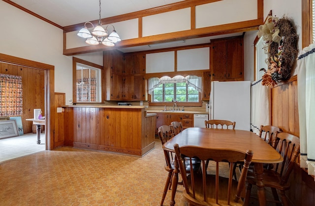 dining room with wood walls, ornamental molding, sink, and a chandelier